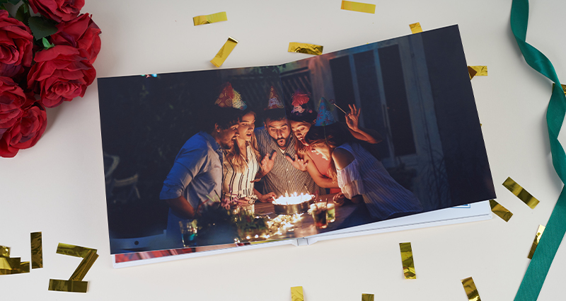 Personalised photo album as a special gift for a 40th birthday - photo of a birthday party with cake, candles and a group of friends, with decorations, confetti and red roses in the background. The perfect gift full of emotions and memories.