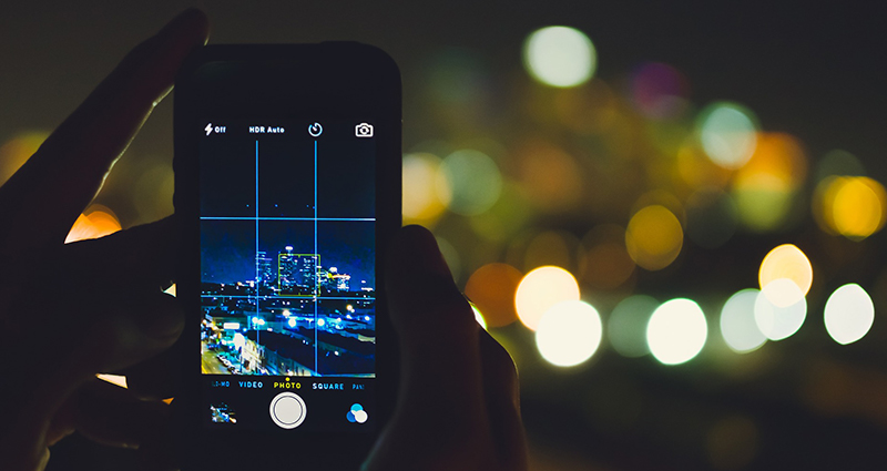 A close up on a smartphone which displays a grid dividing the take into parts, city at night in the background.
