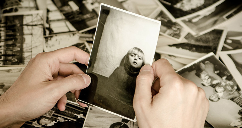 Černo-bílé fotografie položené na psacím stole, detailní záběr na dlaně muže držícího fotku holčičky.
