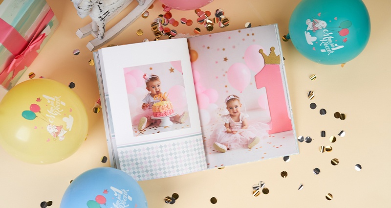 A gift idea for a one-year anniversary - a photo book with photos from a girl's first birthday, embellished with balloons and confetti.