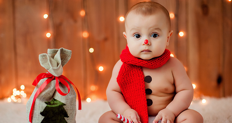 Een in een rode sjaal gewikkelde baby, die naast een cadeau zit