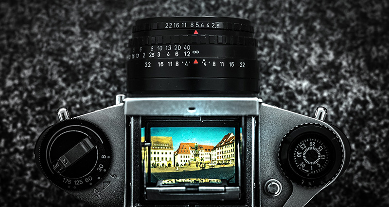 Schwarze Kamera auf Granithintergrund, auf ihrer Anzeige ein buntes Bild eines Gebäudes und blauen Himmels - Foto aus der Vogelperspektive.
