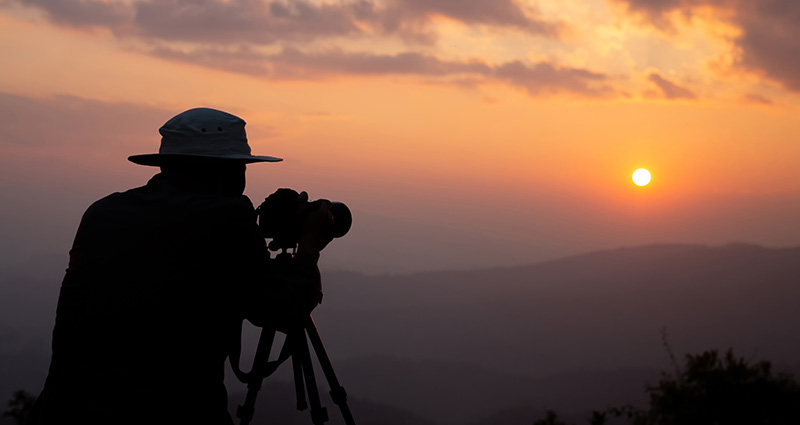 Ein Mann mit dem Hut macht ein Foto beim Sonnenaufgang