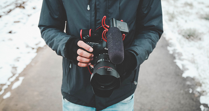 Fotoapparat gehalten von einem Mann mit den fingerlosen Handschuhen