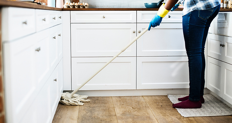 Una donna che lava il pavimento in una cucina composta da mobili bianchi.