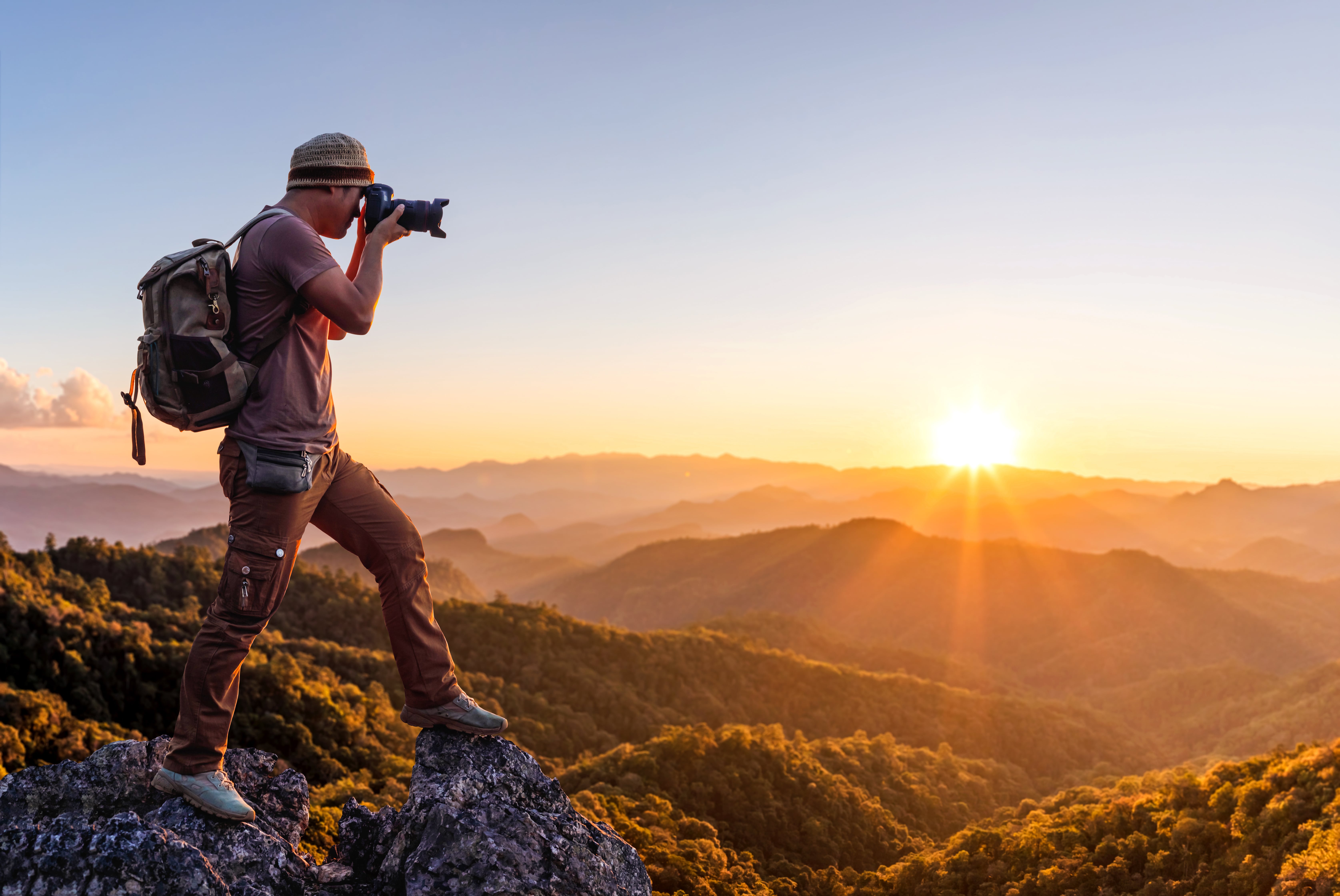 Ein Reisefotograf steht in den Bergen vor dem Sonnenuntergang. Er hat die beste Kamera für Reisefotografie, Ausrüstung, Objektive und eine entsprechende Kleidung besorgt.