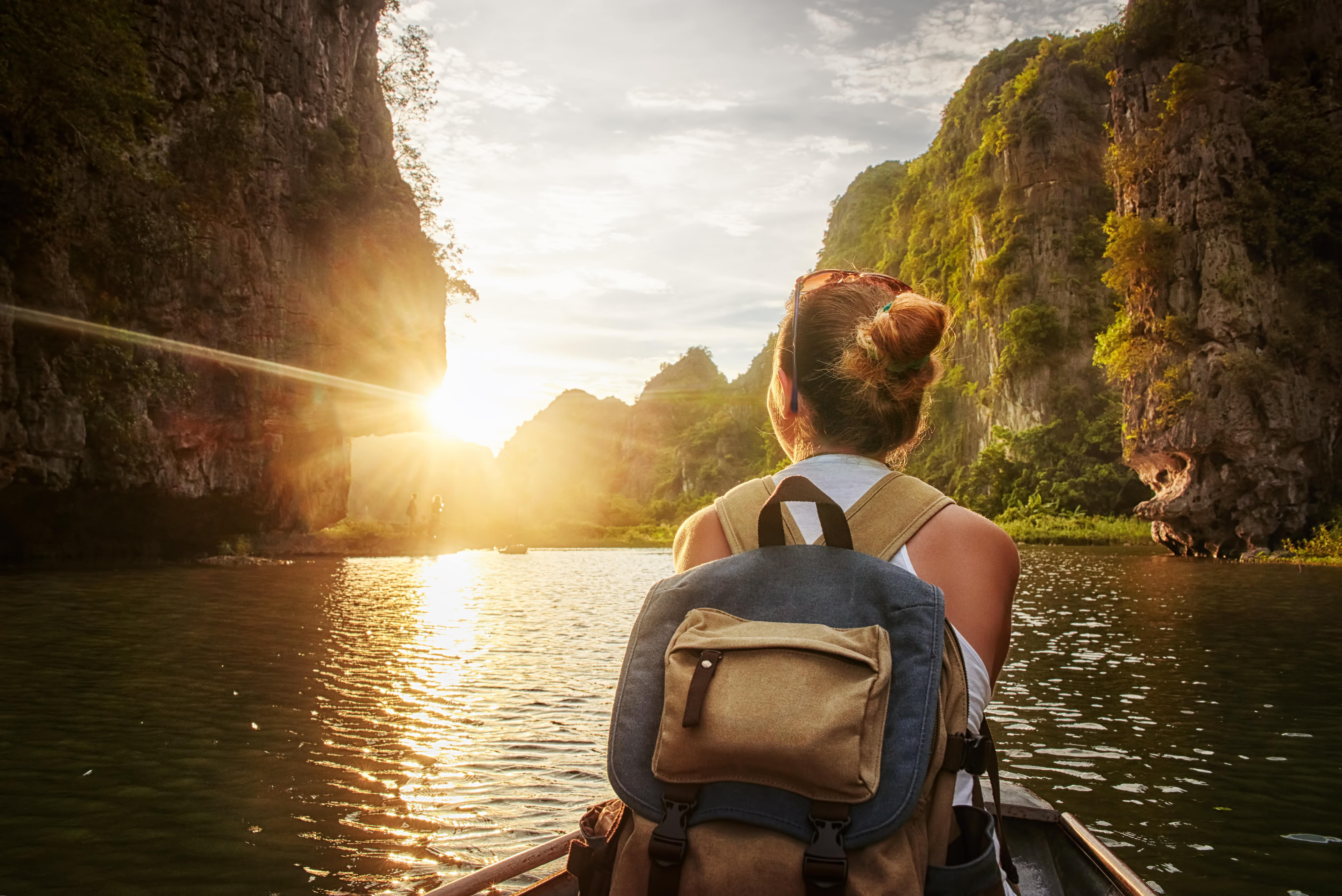 Ein Reisefotograf, eine junge Frau, sitzt in einem Boot, blickt in die Richtung der untergehenden Sonne und wartet auf den richtigen Moment,um tolle Reisefotos zu machen, die dann als ein Reisefotobuch oder Reisemagnete gedruckt werden.