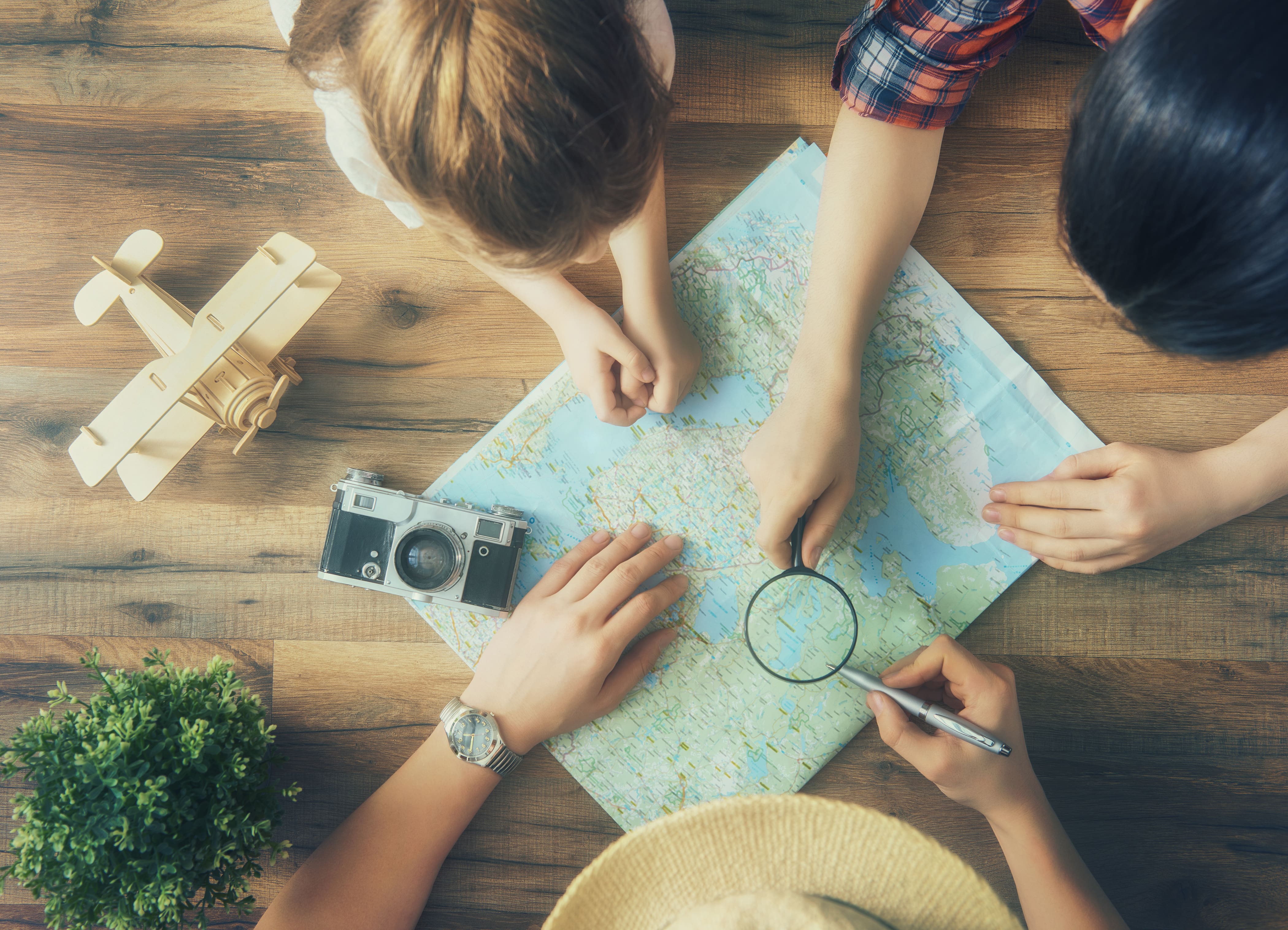 Drei Familienmitglieder beugen sich über eine auf dem Boden ausgebreitete Karte und planen ihren Sommerurlaub.