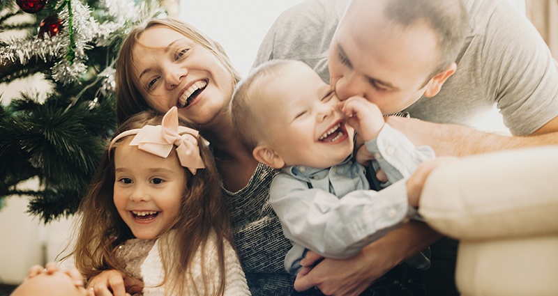 A laughing family playing at Christmas next to a Christmas tree