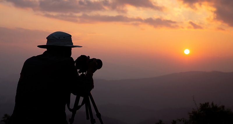 Un hombre en un sombrero tomando una foto durante la salida del sol