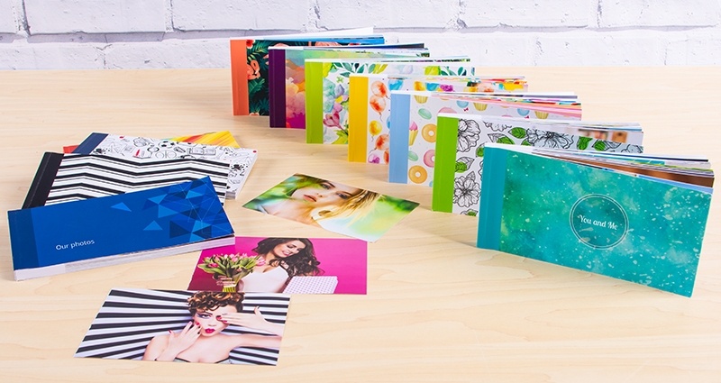 Collection of sharebooks with new covers on a desk, some of them standing in a row on the right side, others lying on the left side. 3 photos loosely located in the middle of the desk, a brick wall in the background.