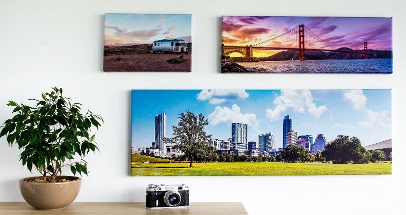 Una colección de tres fotolienzos de paisajes en la pared, una flor sobre un estante al lado.