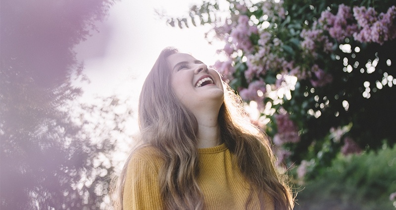 Mujer sonriendo entre los flores de arbustos.